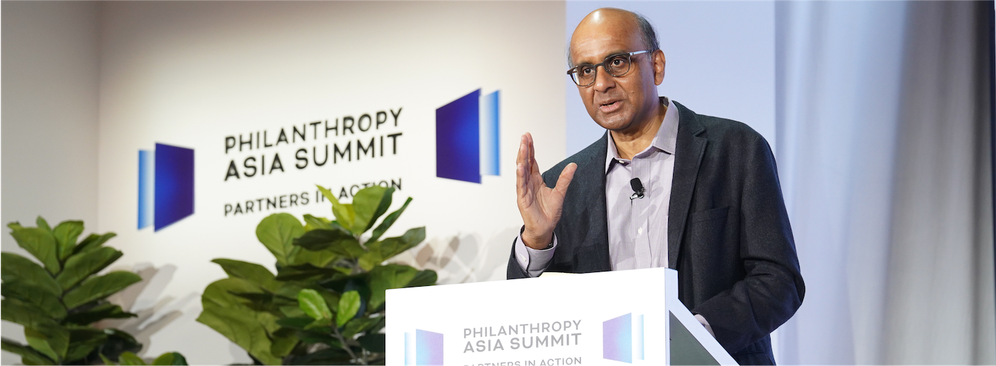 Man at podium speaking at Philanthropy Asia Summit; plants in view.